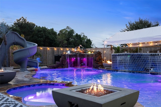 pool at dusk with an in ground hot tub, pool water feature, and an outdoor fire pit