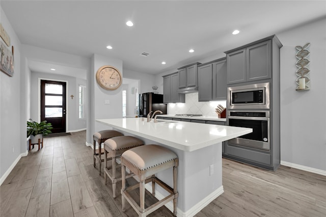 kitchen featuring stainless steel appliances, a kitchen breakfast bar, light hardwood / wood-style floors, gray cabinets, and a kitchen island with sink