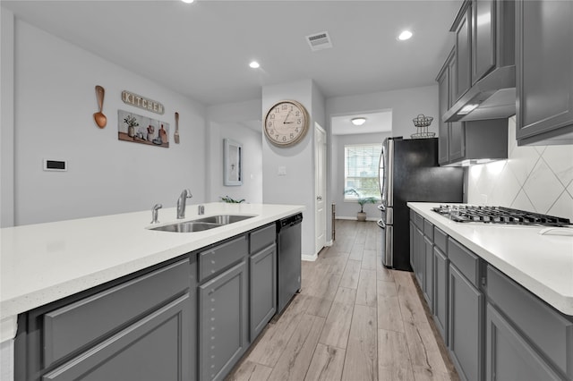 kitchen featuring gray cabinetry, sink, stainless steel appliances, backsplash, and light wood-type flooring