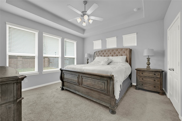 bedroom with ceiling fan, light carpet, and a tray ceiling