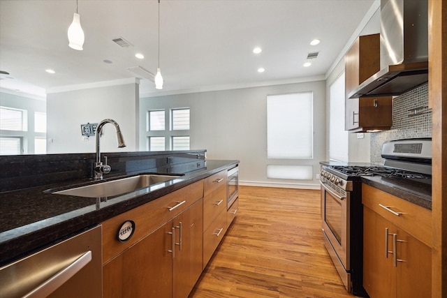 kitchen featuring stainless steel appliances, sink, decorative light fixtures, wall chimney exhaust hood, and ornamental molding