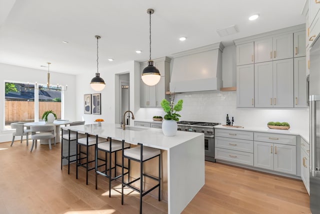 kitchen with a kitchen breakfast bar, sink, premium range hood, a kitchen island with sink, and high end stove