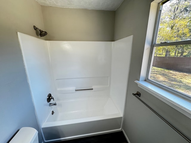 bathroom with shower / bathtub combination, a healthy amount of sunlight, a textured ceiling, and toilet