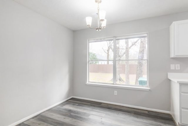 unfurnished dining area with a chandelier, baseboards, and wood finished floors