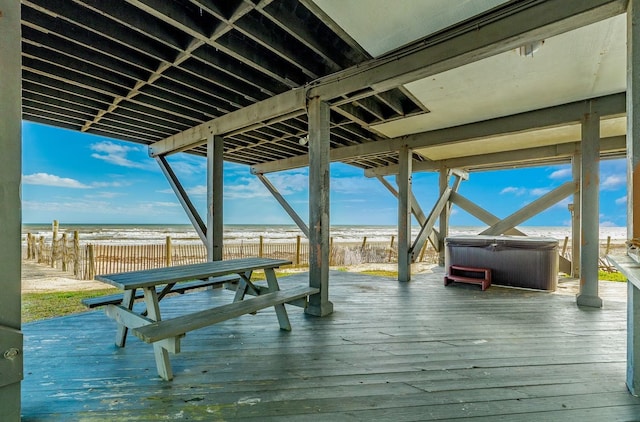 exterior space with a beach view, a deck with water view, and a hot tub