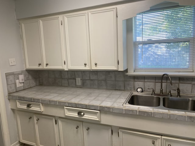 kitchen with tasteful backsplash, white cabinetry, and sink