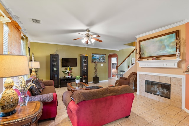 living room featuring ceiling fan, light tile patterned floors, crown molding, and a tile fireplace