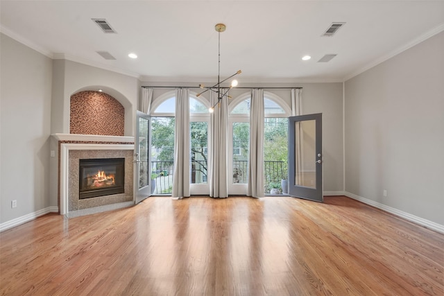 unfurnished living room with a chandelier, french doors, light wood-type flooring, and crown molding