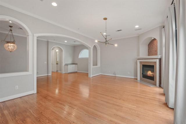 unfurnished living room featuring an inviting chandelier, light hardwood / wood-style floors, and ornamental molding