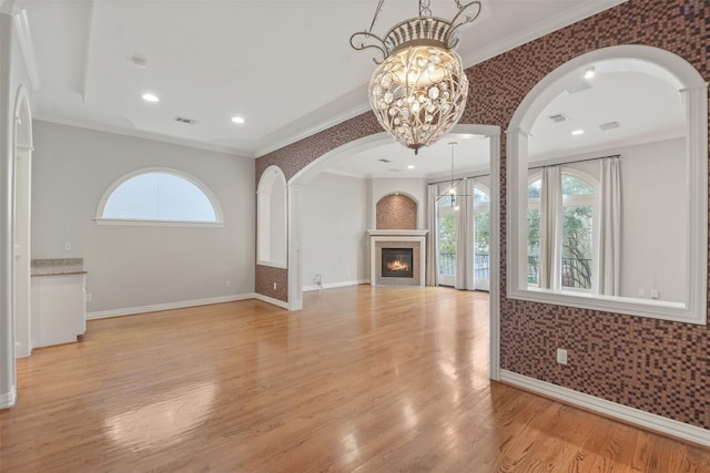 unfurnished living room featuring an inviting chandelier, light hardwood / wood-style flooring, a wealth of natural light, and ornamental molding