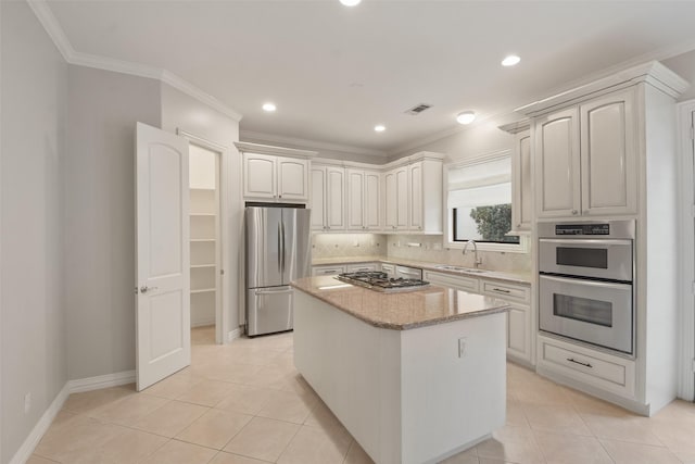 kitchen with sink, tasteful backsplash, light tile patterned flooring, a kitchen island, and appliances with stainless steel finishes