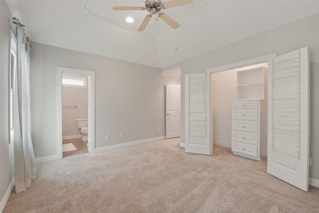 unfurnished bedroom with light carpet, a walk in closet, vaulted ceiling, ensuite bath, and ceiling fan