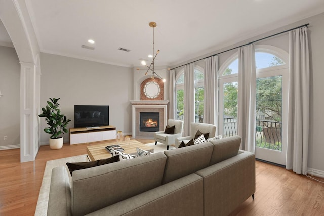 living room featuring crown molding, a fireplace, a chandelier, and light wood-type flooring