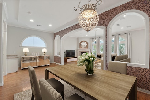 dining space featuring light wood-type flooring, an inviting chandelier, plenty of natural light, and crown molding