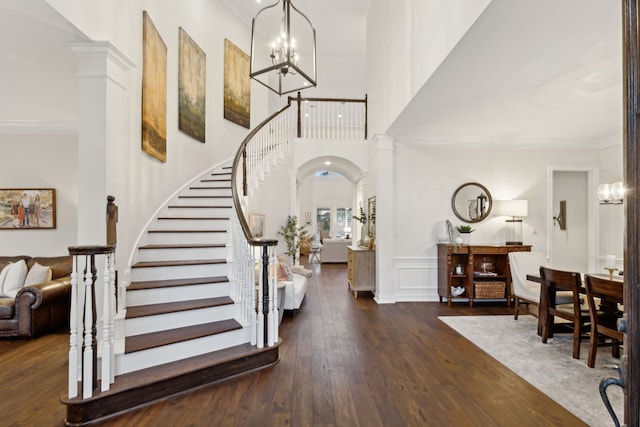 entrance foyer featuring dark hardwood / wood-style flooring, a towering ceiling, ornamental molding, and ornate columns