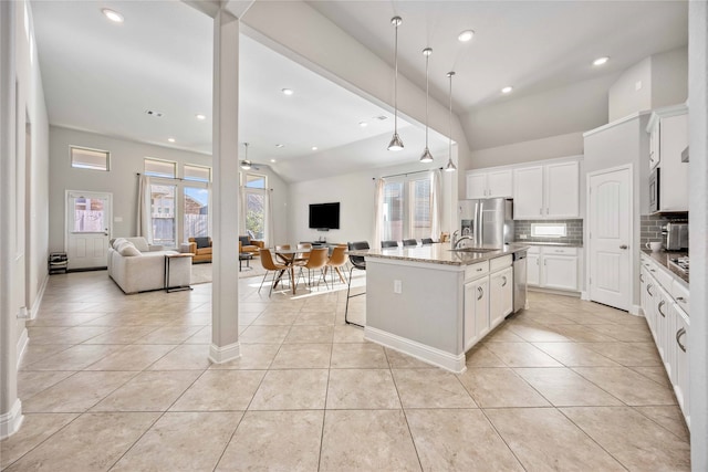 kitchen with light stone countertops, tasteful backsplash, a kitchen island with sink, ceiling fan, and lofted ceiling