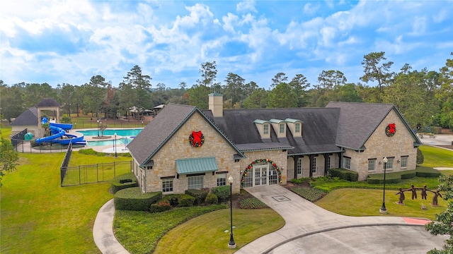 view of front facade featuring a front yard, stone siding, a chimney, french doors, and fence