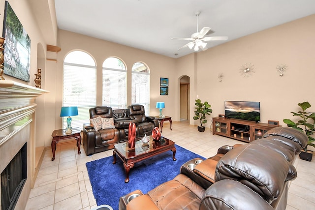 living area featuring a high end fireplace, arched walkways, light tile patterned floors, and ceiling fan