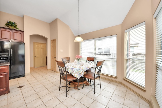 dining space with light tile patterned floors, arched walkways, a healthy amount of sunlight, and vaulted ceiling