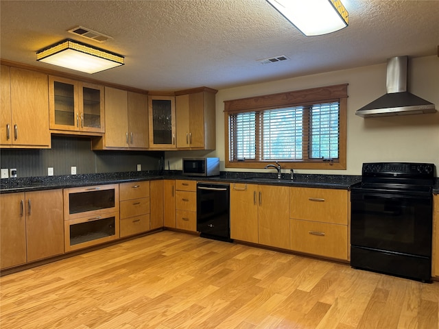 kitchen with light wood-type flooring, a textured ceiling, wall chimney range hood, sink, and black appliances