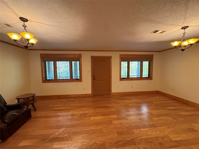 unfurnished living room featuring a healthy amount of sunlight, a textured ceiling, a notable chandelier, and wood-type flooring