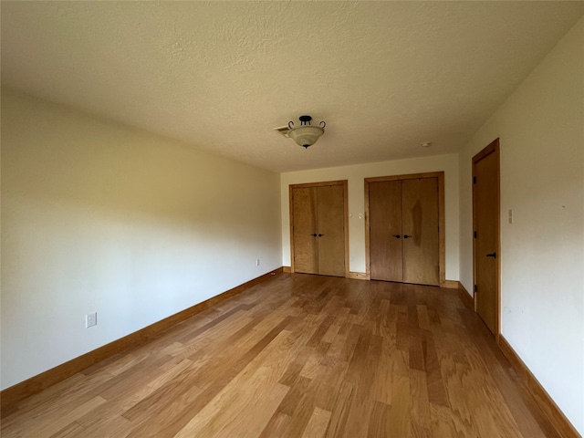 unfurnished bedroom featuring light wood-type flooring, a textured ceiling, and two closets