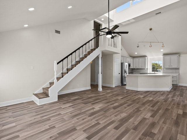 unfurnished living room with ceiling fan, wood-type flooring, sink, and high vaulted ceiling