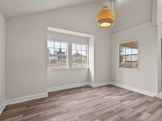 empty room featuring wood-type flooring, vaulted ceiling, and a healthy amount of sunlight