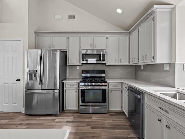 kitchen with backsplash, high vaulted ceiling, wood-type flooring, and appliances with stainless steel finishes