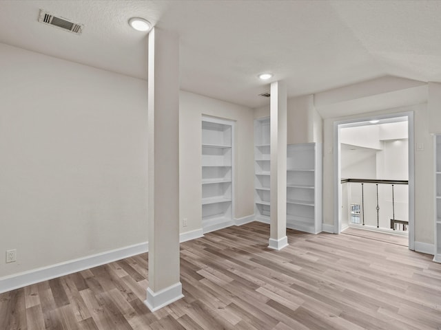 basement featuring built in features, a textured ceiling, and light hardwood / wood-style flooring