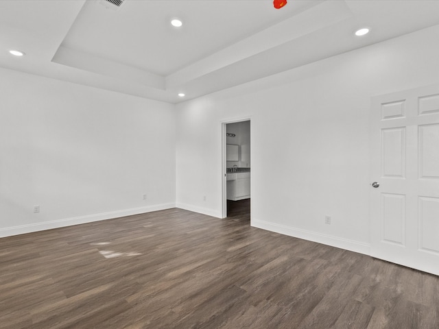 unfurnished bedroom with a tray ceiling, ensuite bath, and dark wood-type flooring