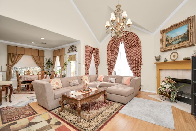 living room featuring crown molding, high vaulted ceiling, an inviting chandelier, light hardwood / wood-style flooring, and a tiled fireplace