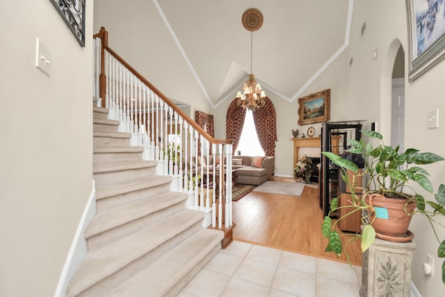 foyer entrance with a notable chandelier, light wood-type flooring, high vaulted ceiling, and a tiled fireplace