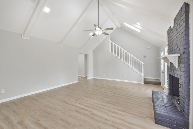 unfurnished living room with a skylight, ceiling fan, a fireplace, beamed ceiling, and light hardwood / wood-style floors