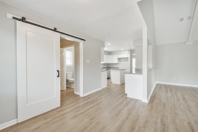 unfurnished living room with a barn door and light hardwood / wood-style flooring