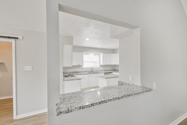 kitchen featuring white cabinets, sink, light stone countertops, light hardwood / wood-style floors, and kitchen peninsula