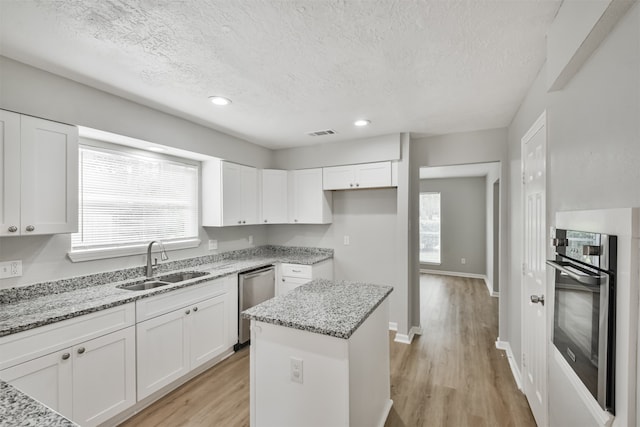 kitchen with white cabinets, black oven, light stone countertops, and sink