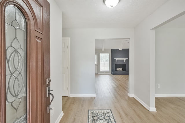 foyer entrance with beam ceiling, light hardwood / wood-style flooring, and a brick fireplace