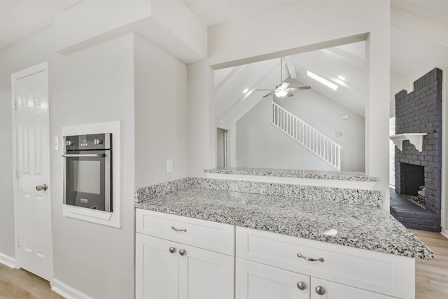 kitchen with kitchen peninsula, ceiling fan, white cabinetry, light hardwood / wood-style flooring, and oven