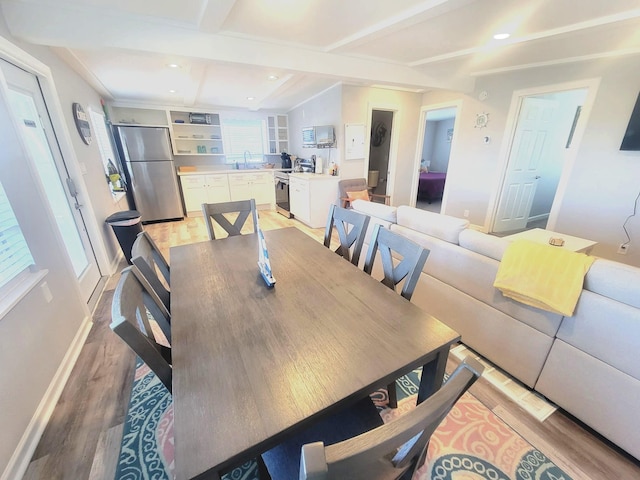 dining space with beam ceiling, built in shelves, sink, and light hardwood / wood-style flooring