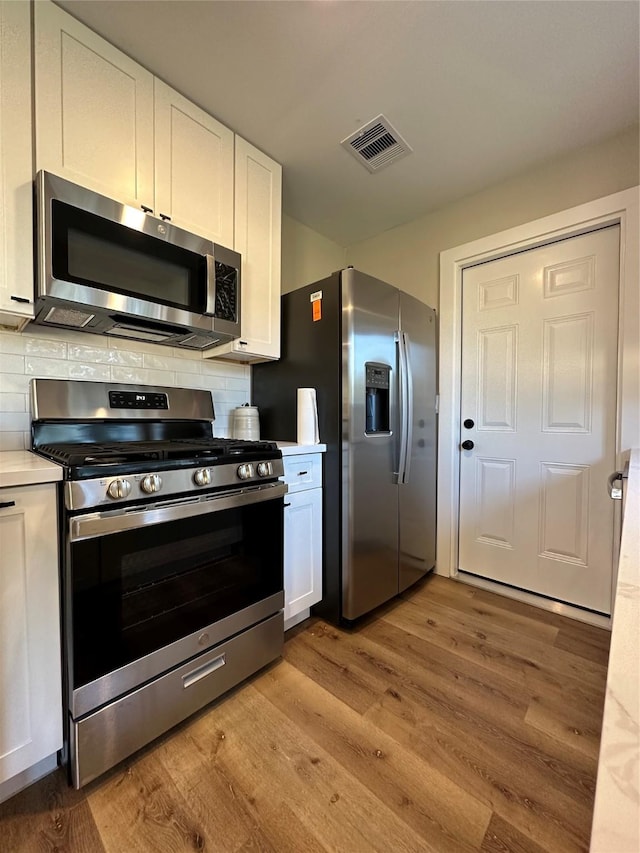 kitchen with backsplash, white cabinets, stainless steel appliances, and light hardwood / wood-style floors