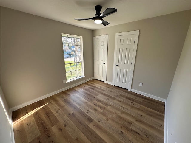 unfurnished bedroom with ceiling fan, wood-type flooring, and two closets