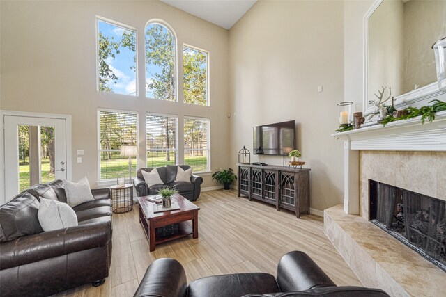 living room with a towering ceiling, light wood-type flooring, and a premium fireplace