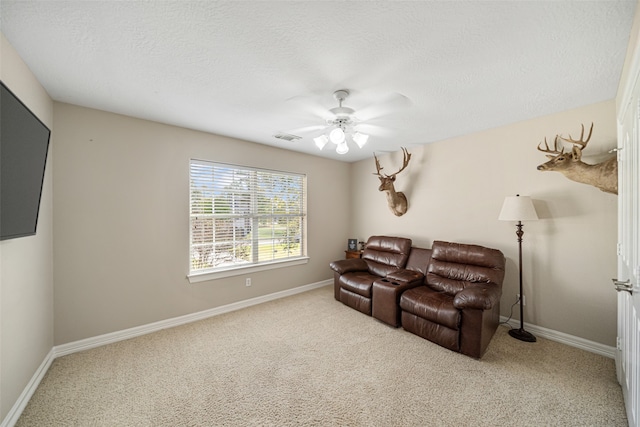 home theater room featuring ceiling fan, light colored carpet, and a textured ceiling