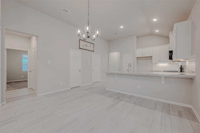 kitchen featuring white cabinetry, light hardwood / wood-style floors, lofted ceiling, decorative light fixtures, and a breakfast bar area