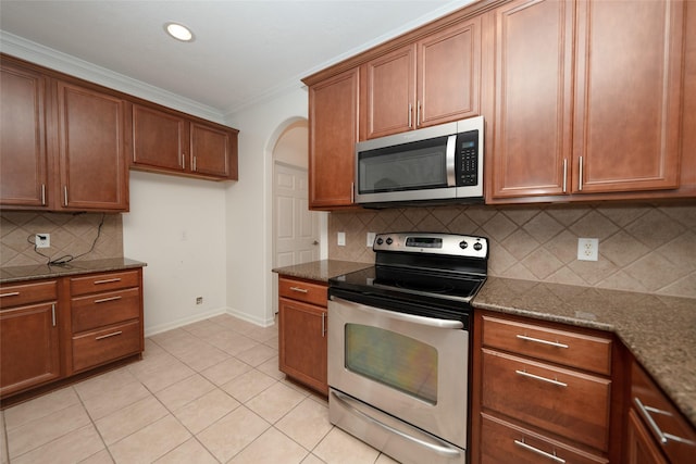 kitchen featuring appliances with stainless steel finishes, backsplash, ornamental molding, light tile patterned floors, and dark stone countertops