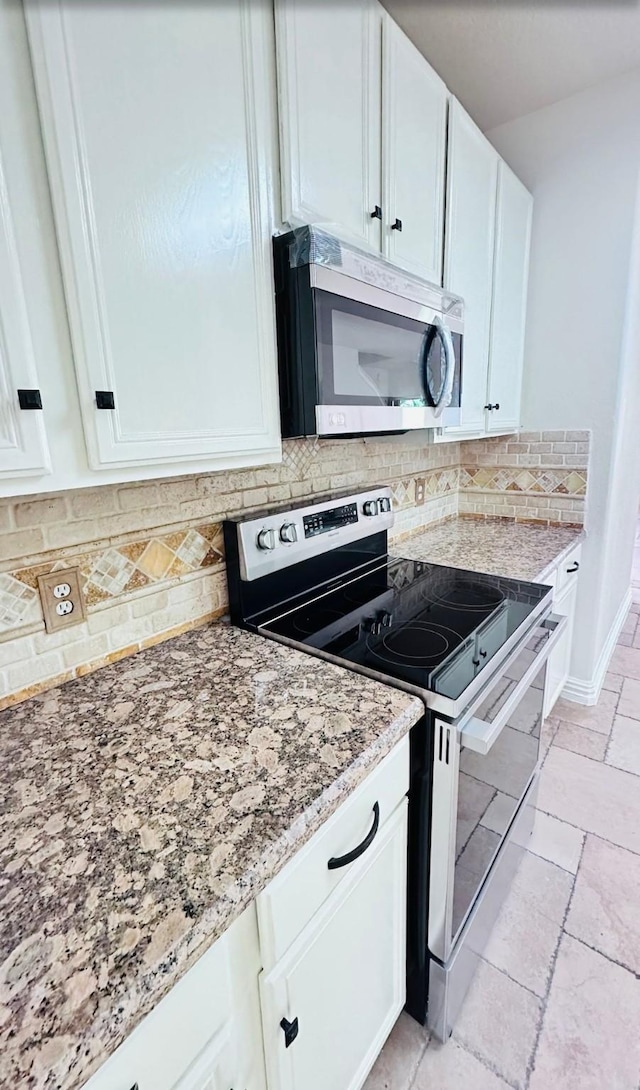 kitchen with white cabinets, appliances with stainless steel finishes, tasteful backsplash, and light stone countertops