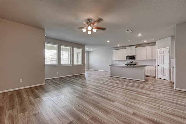 unfurnished living room with a textured ceiling, light wood-type flooring, ceiling fan, and sink