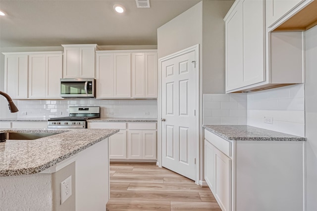 kitchen with white cabinets, sink, light wood-type flooring, light stone counters, and stainless steel appliances