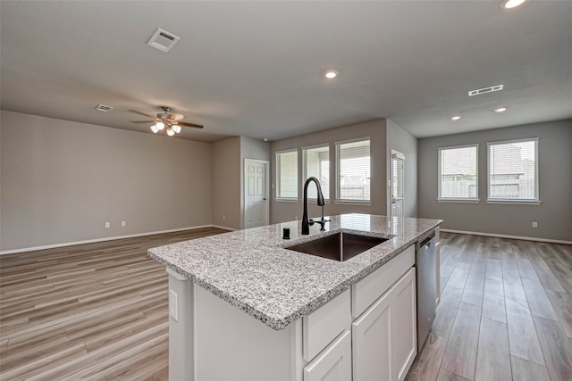 kitchen with light wood-type flooring, stainless steel dishwasher, a kitchen island with sink, sink, and white cabinetry